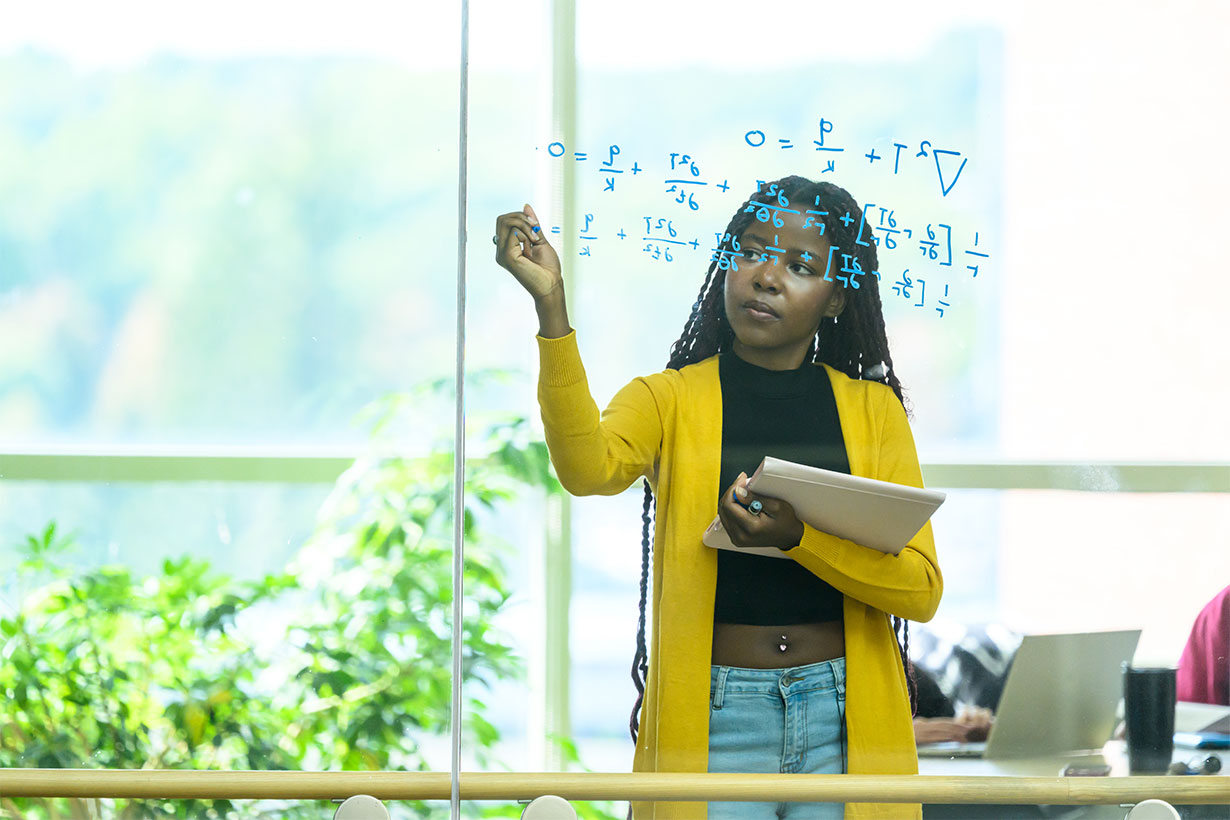 Woman writing on glass in a yellow sweater.