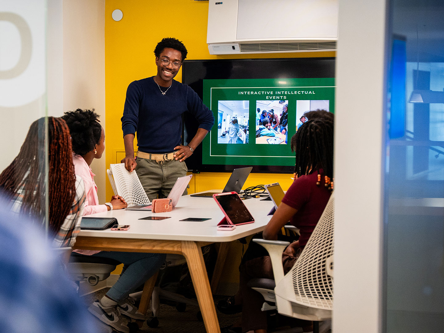 Man teaching students in a small classroom with interactive intellectual events on the screen.