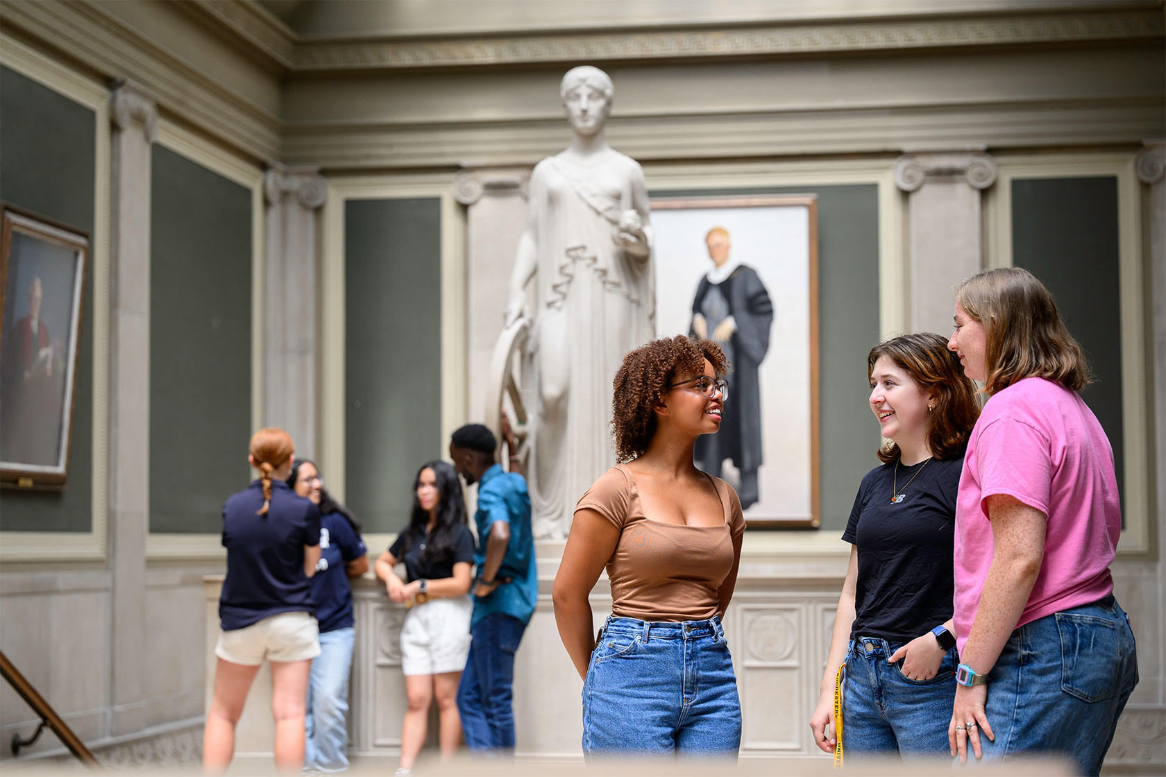 Three women talking in front of a statue inside Rush Rhees library.